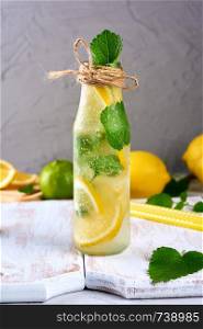 summer refreshing drink lemonade with lemons, mint leaves, lime in a glass bottle, next to the ingredients for making a cocktail