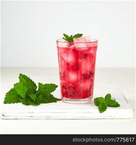 summer refreshing drink with berries of cranberries and pieces of ice in a glass on a wooden board, white background