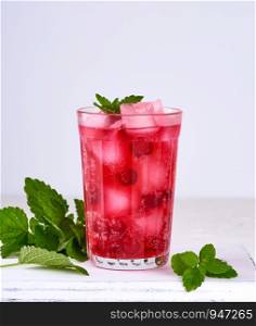 summer refreshing drink with berries of cranberries and pieces of ice in a glass on a wooden board, white background