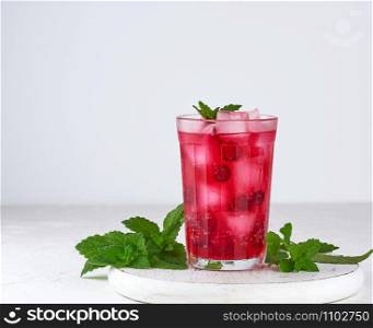 summer refreshing drink with red berries of cranberries and pieces of ice in a glass on a wooden board, white background