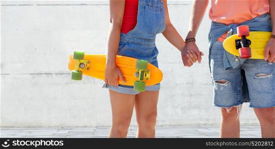 summer, relations, extreme sport and people concept - close up of happy teenage couple with short modern cruiser skateboards over urban background. close up of young couple with skateboards outdoors