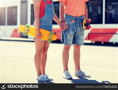 summer, relations, extreme sport and people concept - close up of happy teenage couple with short modern cruiser skateboards on city street. close up of young couple with skateboards in city