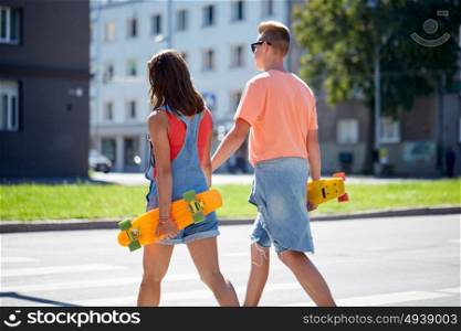 summer, relations, traffic, extreme sport and people concept - happy teenage couple with short modern cruiser skateboards crossing city crosswalk. teenage couple with skateboards on city crosswalk