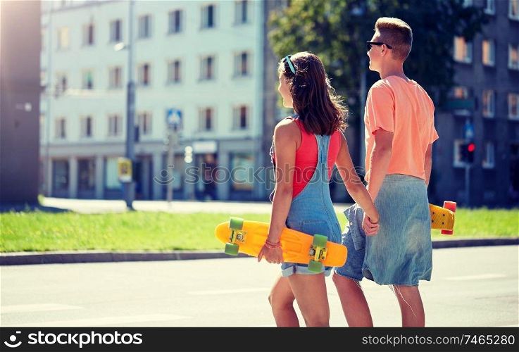 summer, relations, traffic, extreme sport and people concept - happy teenage couple with short modern cruiser skateboards crossing city crosswalk. teenage couple with skateboards on city crosswalk