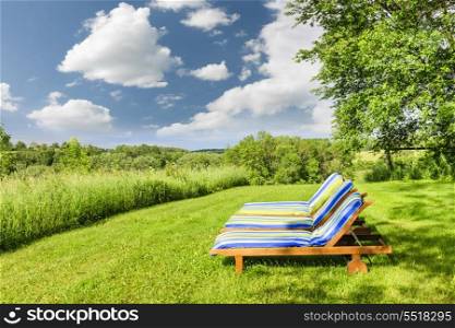 Summer relaxing. Two wooden outdoor lounge chairs on lush green lawn with trees