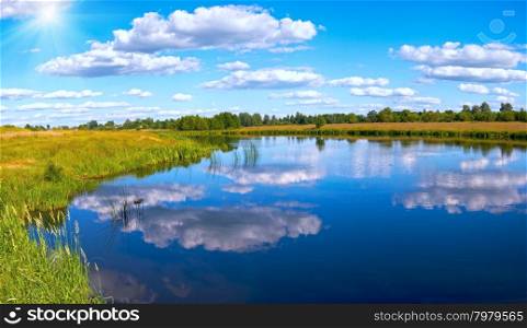 Summer rushy lake panorama view with clouds reflections and sunshine.