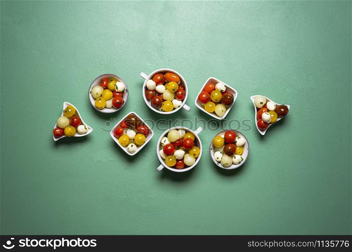 Summer salad with cherry tomatoes, melon and mozzarella balls in many bowls. Salad portions on a green background. Above view of Caprese salad.