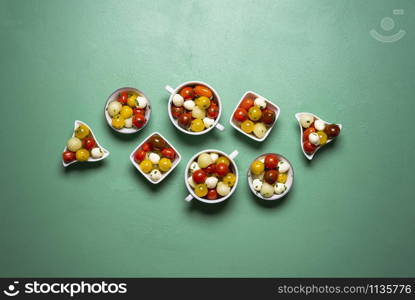 Summer salad with cherry tomatoes, melon and mozzarella balls in many bowls. Salad portions on a green background. Above view of Caprese salad.