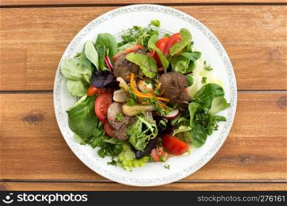 Summer salad with fried rabbit liver and fresh vegetables on a wooden table.