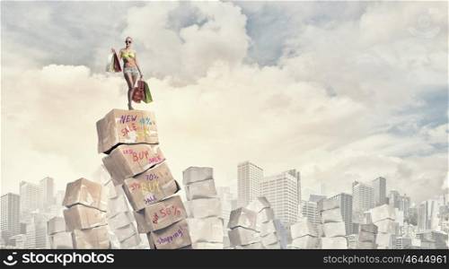Summer sale. Beautiful young girl in bikini with shopping bags on pile of carton boxes