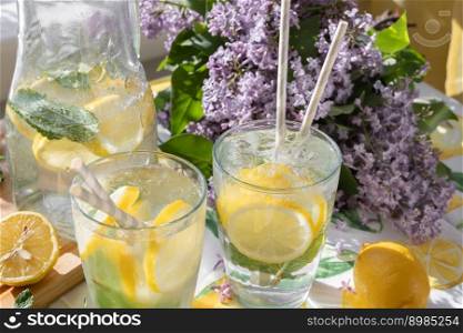 Summer scene of iced-cold lemon soda water next to a window. Sunlight comes from the window. Lilac flowers on the background. Two glasses with iced-cold limonade