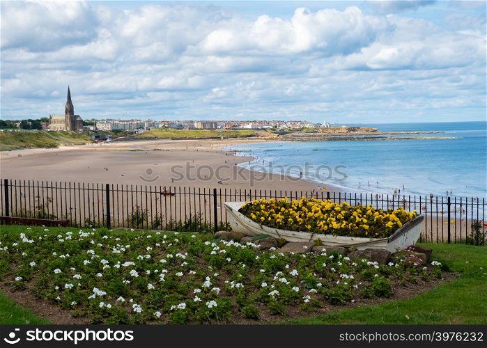 Summer scene of Ornamental Boat containing Flowers, with Tynemouth&rsquo;s Coastline in the background