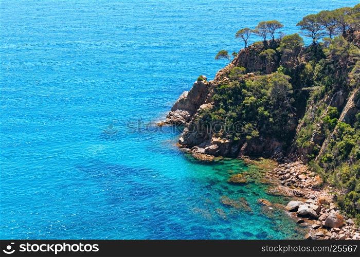Summer sea rocky coast view with boat and sunny sparkles on water surface (Spain).