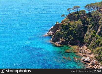 Summer sea rocky coast view with boat and sunny sparkles on water surface (Spain).