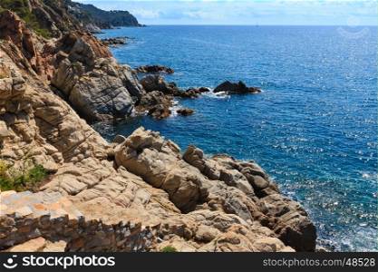 Summer sea rocky coast view with sunny sparkles on water surface and stony stairs (Costa Brava, Spain).
