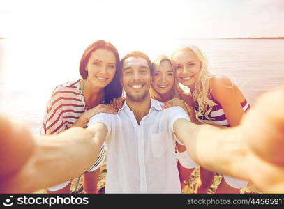 summer, sea, tourism, technology and people concept - group of smiling friends with camera on beach photographing and taking selfie