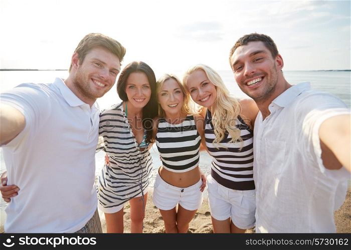 summer, sea, tourism, technology and people concept - group of smiling friends with camera on beach photographing and taking selfie