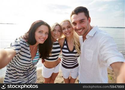 summer, sea, tourism, technology and people concept - group of smiling friends with camera or smartphone photographing and taking selfie on beach