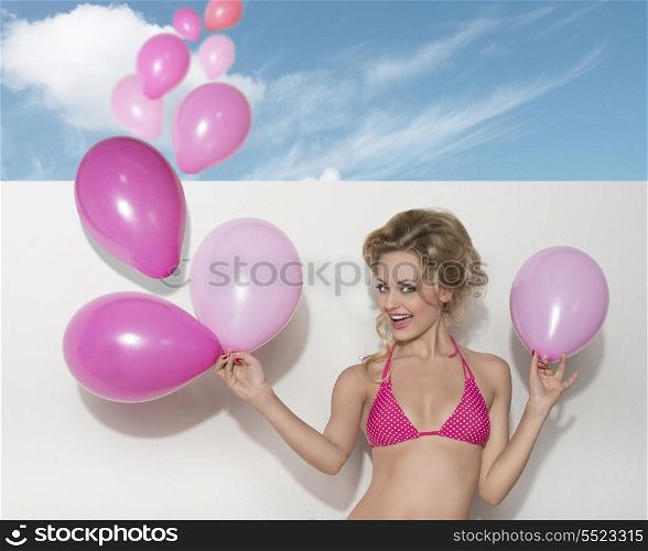 summer shoot of blonde female with pink swimwear and pink balloons, smiling and looking in camera. Funny expression.