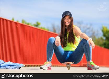Summer sport and active lifestyle. Cool teenage girl skater sitting on skateboard on the street. Outdoor.