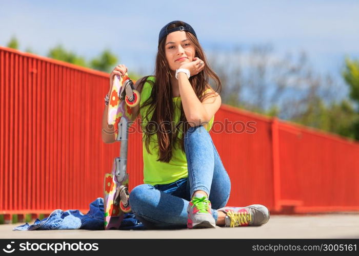 Summer sport and active lifestyle. Cool teenage girl skater sitting with skateboard on the street. Outdoor.