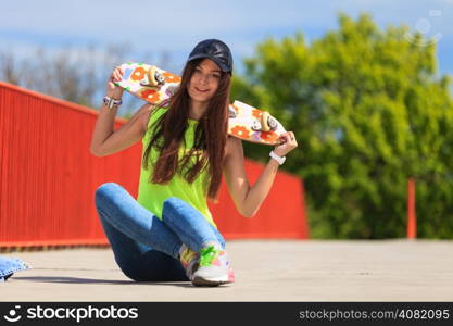 Summer sport and active lifestyle. Cool teenage girl skater sitting with skateboard on the street. Outdoor.