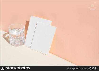 summer stationery mock-up scene. Blank business card and glass of clear water on beige textured table background.. summer stationery mock-up scene.