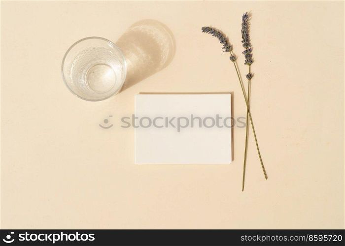 summer stationery mock-up scene. Blank business card with lavender flowers and glass of water on beige textured table background. Flat lay, top view. summer stationery mock-up scene.