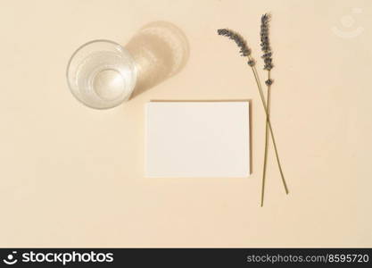 summer stationery mock-up scene. Blank business card with lavender flowers and glass of water on beige textured table background. Flat lay, top view. summer stationery mock-up scene.