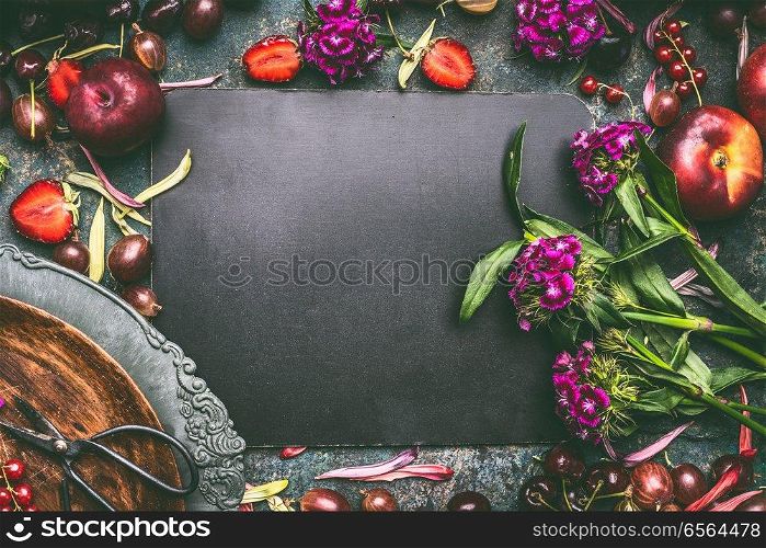 Summer still life background with fresh berries, fruits and flowers around blank chalkboard with copy space for your text or design, top view. Country style. Organic food
