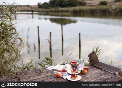 Summer still life- picnic on a wooden pier. wine, sinabones, peaches, a book with a lake view