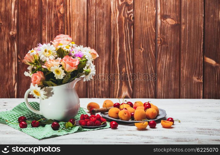 Summer still life with peaches, raspberries, cherries and flowers on a wooden table