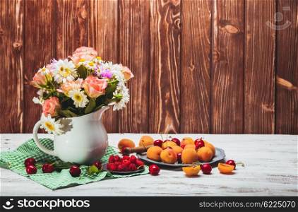 Summer still life with peaches, raspberries, cherries and flowers on a wooden table