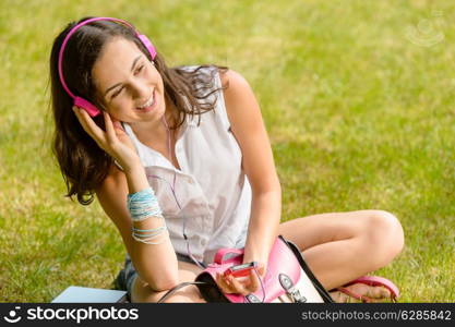 Summer student girl listening to music sitting on grass smiling