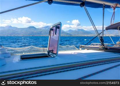 Summer sunny day aboard a sailing yacht. Rigging and mast. View of the hilly coast. View From the Side of a Sailing Yacht on a Hilly Coast