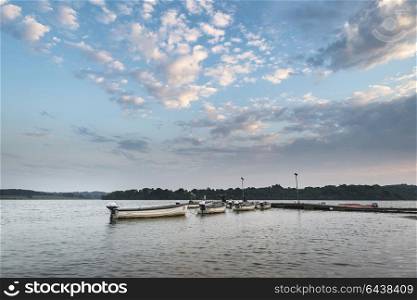Summer sunset landscape image over lake with leisure boats on jetty.