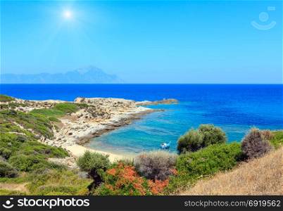 Summer sunshine stony sea coast landscape with Athos mount view in far (Halkidiki, Sithonia, Greece).