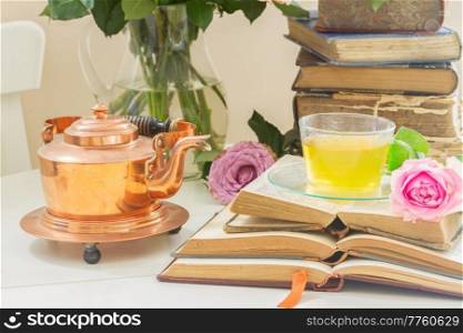 Summer teatime - cup of tea in glass with old books, rose flower and teapot. Cup of tea with books