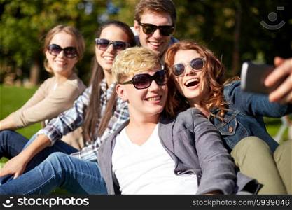 summer, technology, education and teenage concept - group of happy students or teenagers with smarphone taking selfie at campus