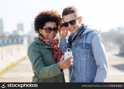 summer, technology, people and friendship concept - smiling couple with smartphone and earphones listening to music on city street