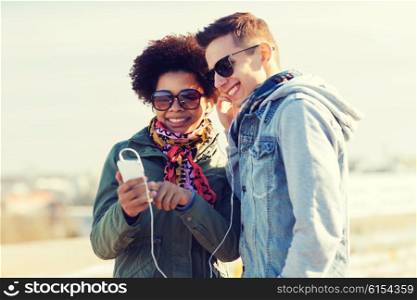 summer, technology, people and friendship concept - smiling couple with smartphone and earphones listening to music on city street