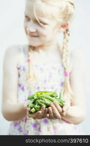 summer - the smiling girl is holding a green peas in her hands