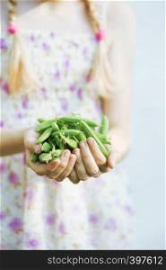 summer - the smiling girl is holding a green peas in her hands