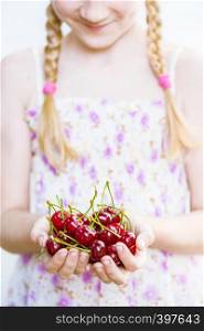 summer - the smiling girl is holding a ripe red cherry in her hands