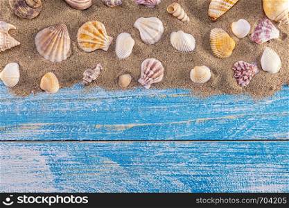 Summer time concept with sea shells on a blue wooden background and sand. Seashells frame on wooden background nautical border. Focus on seashells.