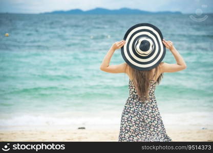 Summer time tan woman vacation on the beach. Cheerful woman wear summer dress and straw hats sitting on the beach look at sea. Time to relax in summer lifestyle outdoor shot on tropical island beach.