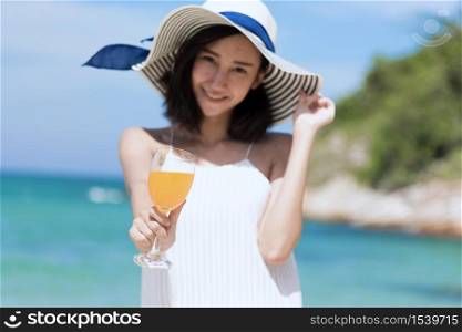 Summer time woman vacation on the beach. Cheerful woman wear summer dress and straw hats sitting on the beach look at sea. Time to relax in summer lifestyle outdoor shot on tropical island beach.