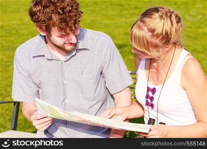 Summer tourism concept. Young tourist couple two friends on vacation in city looking up directions on map, sitting on bench at sunny day. Tourist couple in city read map