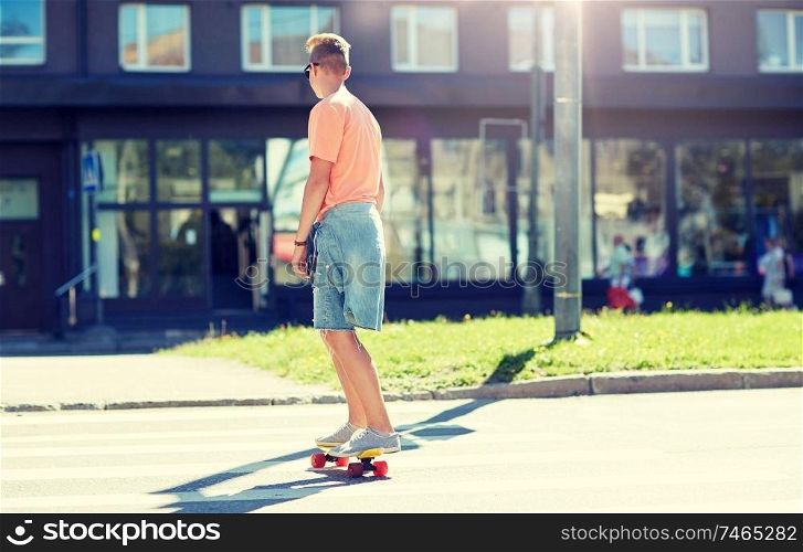 summer, traffic, extreme sport and people concept - teenage boy riding short modern cruiser skateboard on crosswalk in city. teenage boy on skateboard crossing city crosswalk