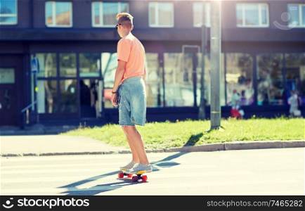 summer, traffic, extreme sport and people concept - teenage boy riding short modern cruiser skateboard on crosswalk in city. teenage boy on skateboard crossing city crosswalk